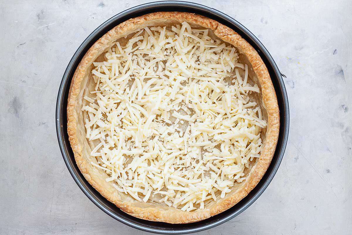 A springform pan with a golden brown crust has shredded mozzarella cheese at the bottom of it.