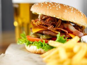 A close-up view of a gourmet hamburger with fries and a glass of beer in the background