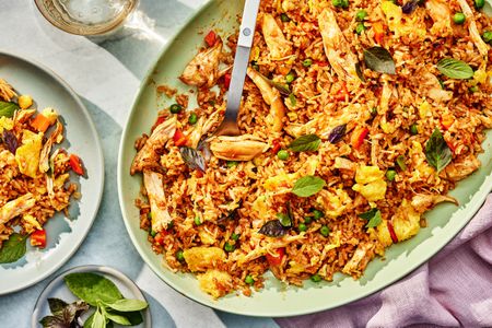 Thai-style fried rice on a platter at a table setting with a serving of fried rice on a plate, a small plate with Thai basil, a glass of water, and a table napkin