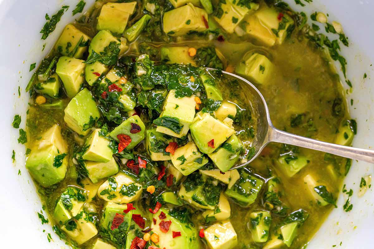 Avocado chimichurri to accompany skirt steak being lifted out of the bowl with a spoon