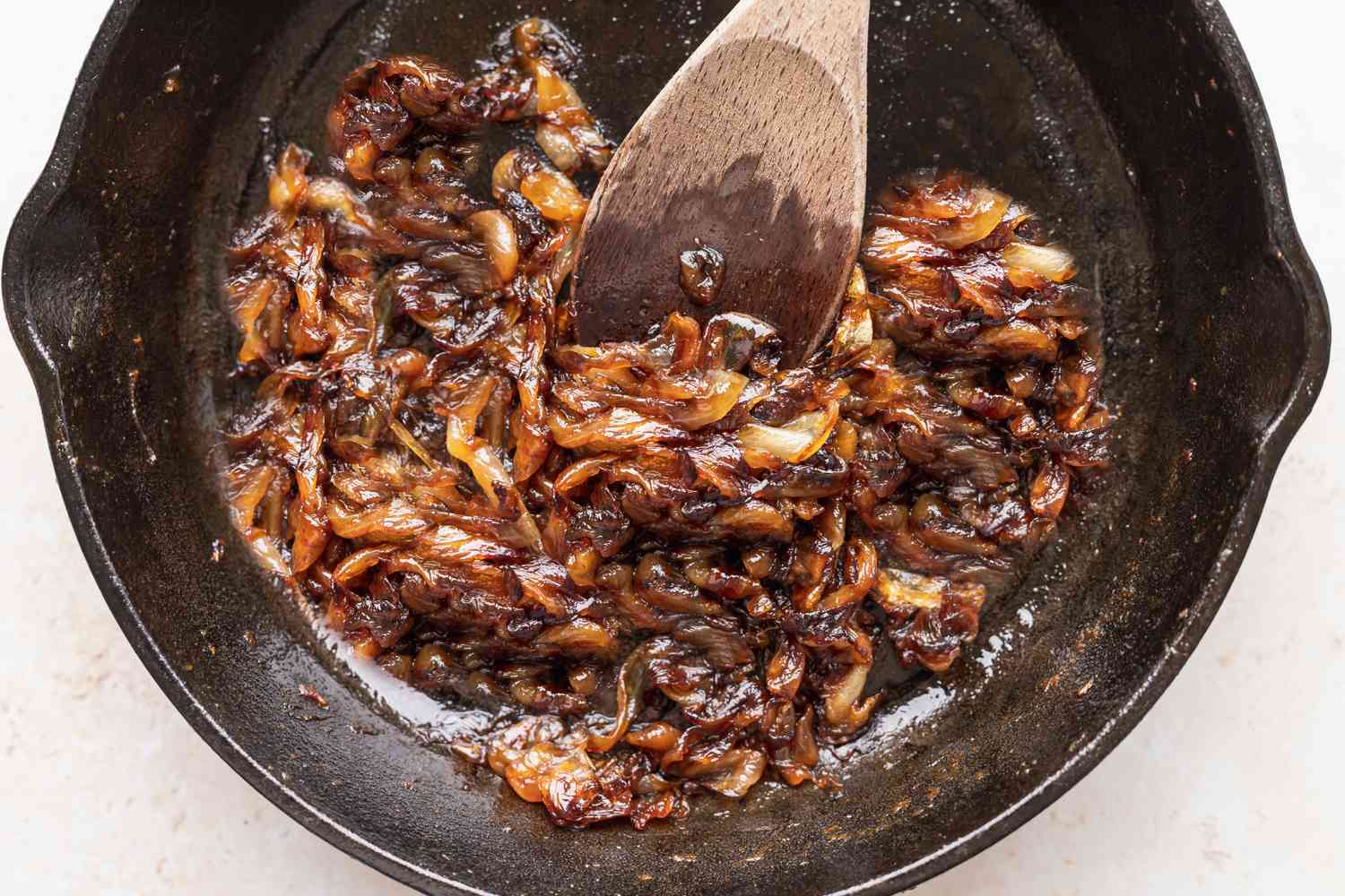 Caramelized onions in a cast iron skillet being stirred by a wooden spoon.
