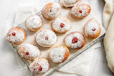 Sufganiyot (Israeli Jelly Donuts) on a Lined Cooling Rack Sitting on Parchment Paper and Next to a Knit Fabric 