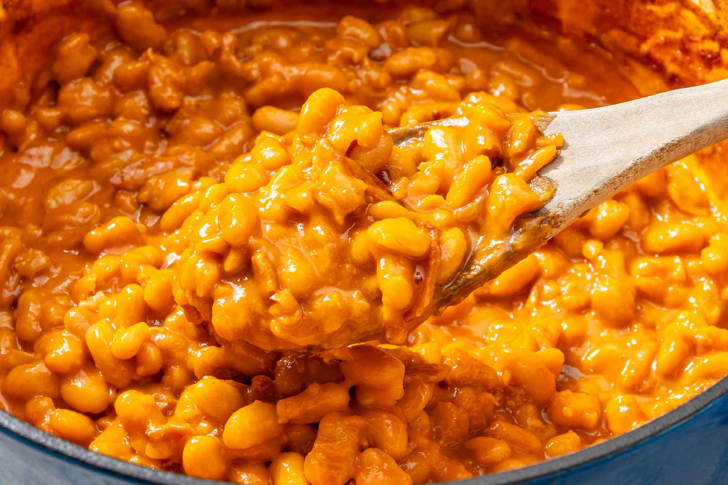 Baked beans being stirred with a wooden spoon in a pan