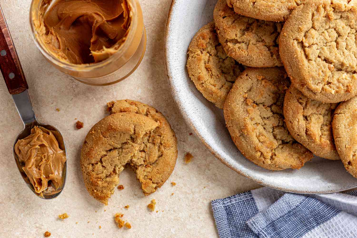 peanut butter cookies (some on a plate and some on the counter) next to a jar of peanut butter 