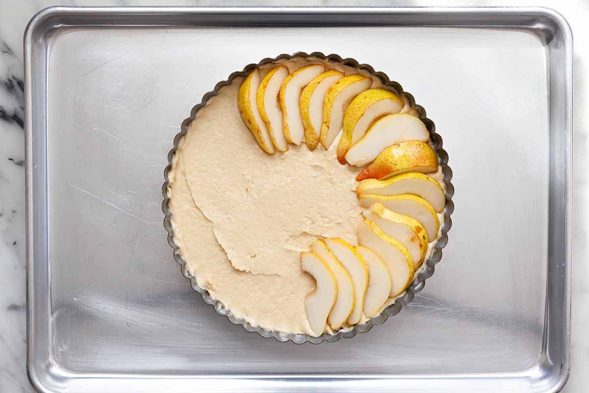 Easy Pear cake batter in a fluted tart tin with sliced pears partially arranged on top
