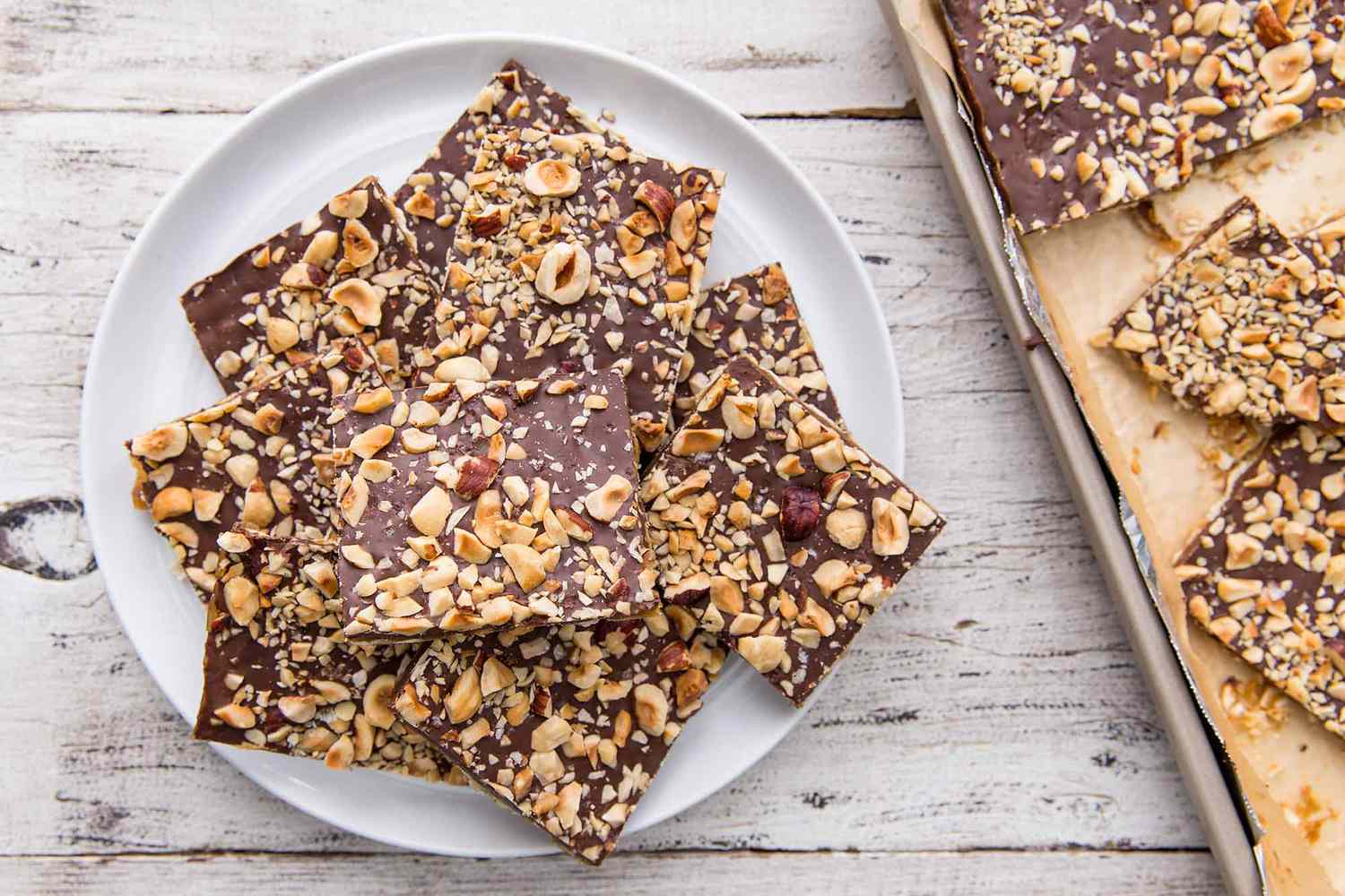 Chocolate Toffee Matzo Crack - plate of toffee wiht sheetpan of toffee in the background