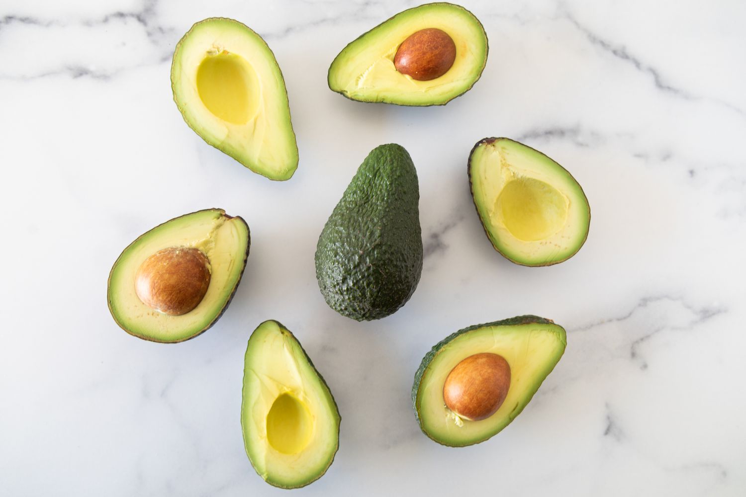 Halved Avocados on a Counter with One Whole Avocado in the Middle 