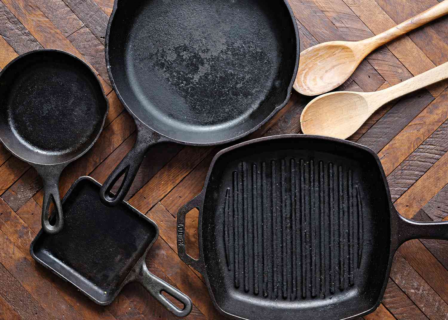 How to Season a Cast Iron Pan - cast iron skillets on a wooden table with wooden spoons nearby