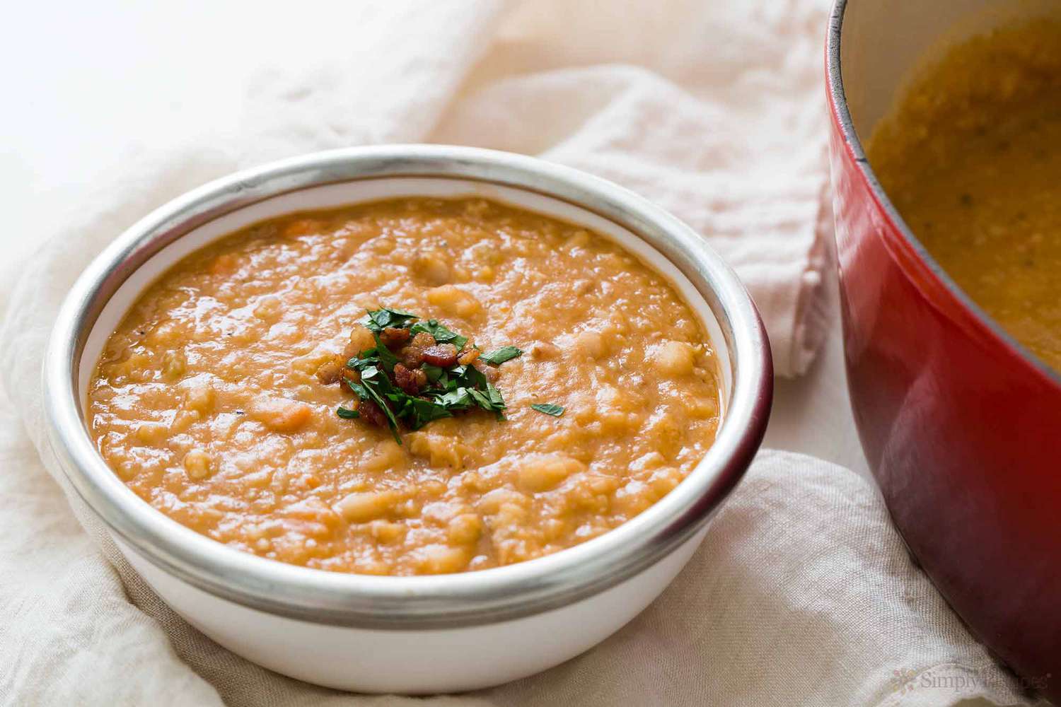 A bowl of white Bean and Bacon Soup with a Dutch oven next to it