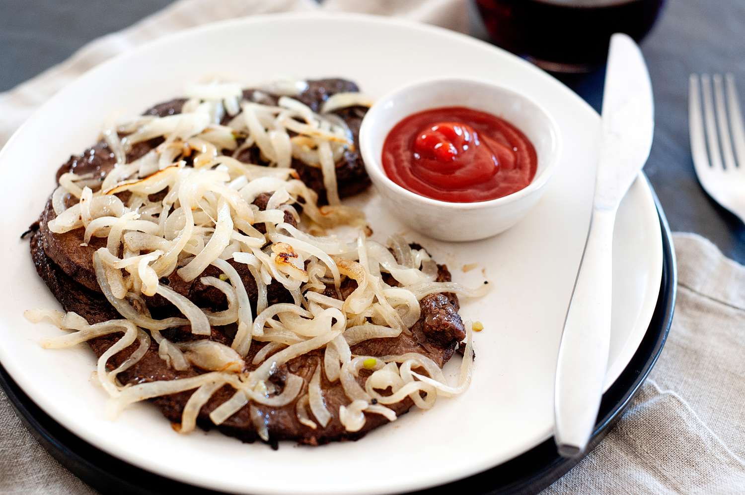 A plate of liver and onions and ketchup.
