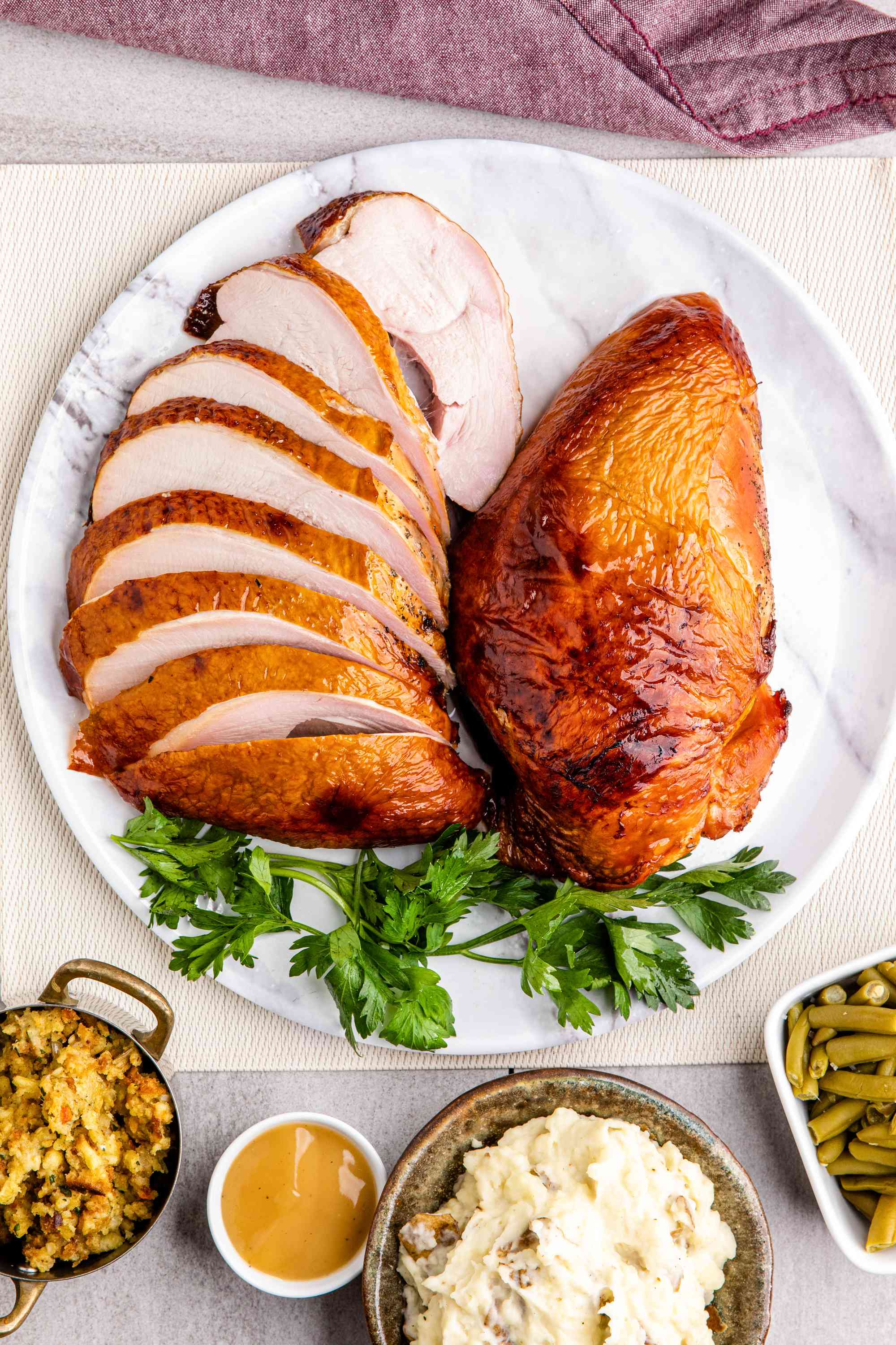 Smoked Thanksgiving turkey breast, one breast sliced, the other whole, on a platter with other Thanksgiving side dishes
