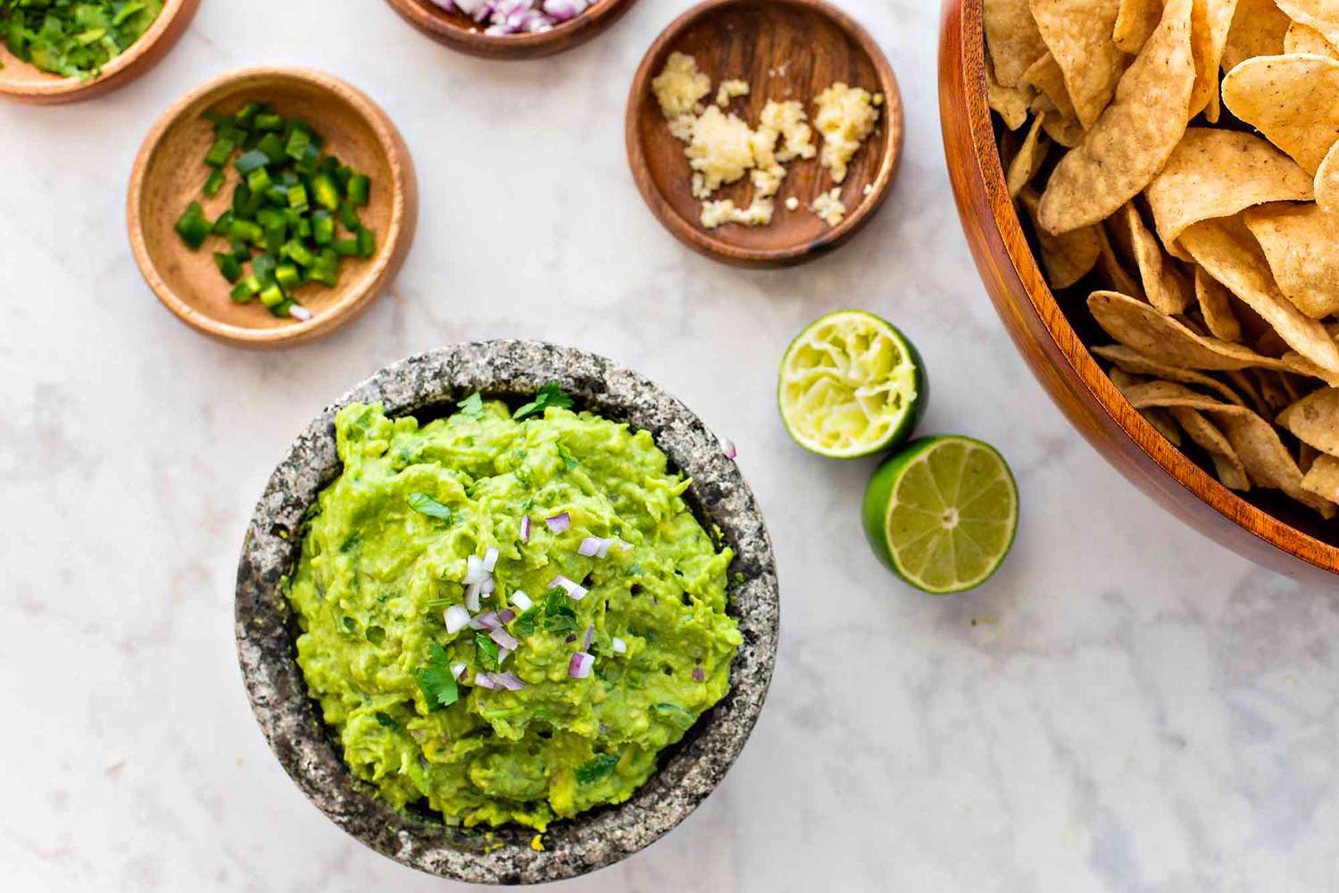 Bright green guacamole in a stone molcajete with a bowl of tortilla chips on the side