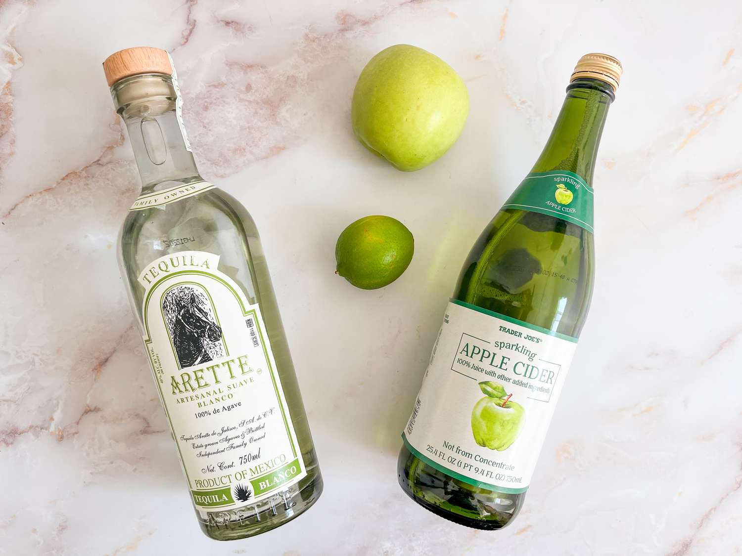 Overhead view of a green apple, lime and bottles of Trader Joe's Sparkling Apple Cider and Arette Tequila