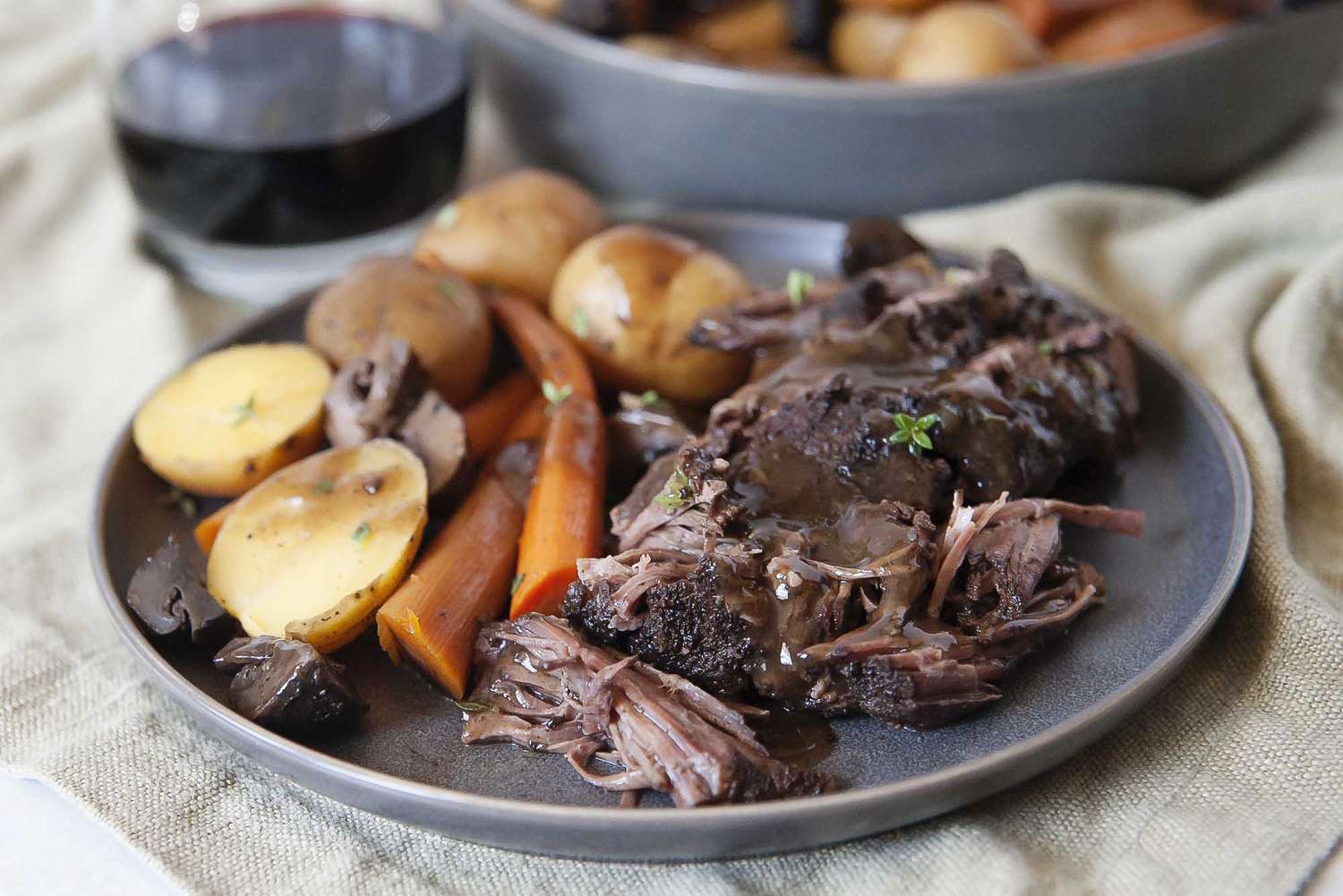 Perfectly tender crock pot roast piled onto a gray plate with carrots and potatoes and covered in gravy.