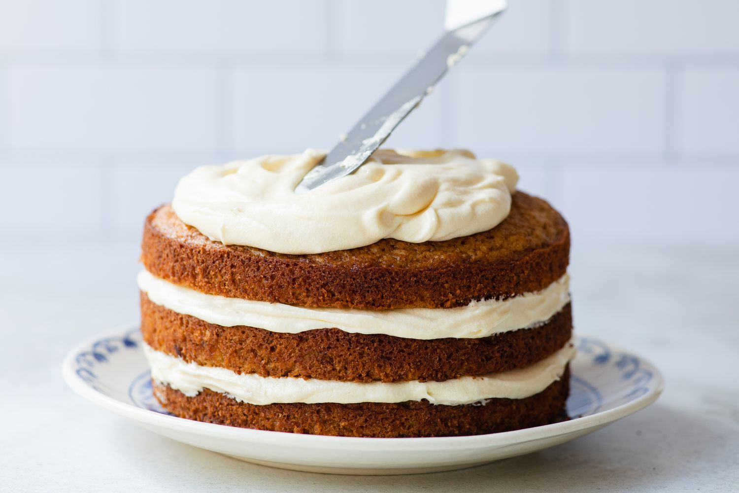 Spreading Homemade Cream Cheese Frosting with a spatula on a layer cake