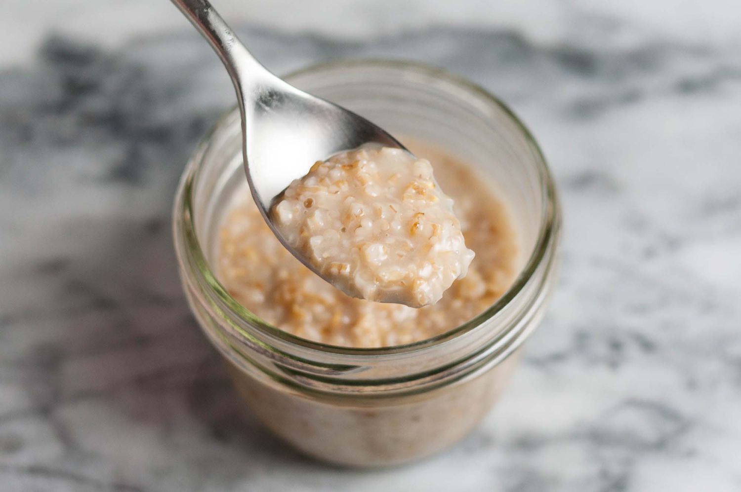 A spoon with creamy still cut oats lifted above a jar of steel cut oats