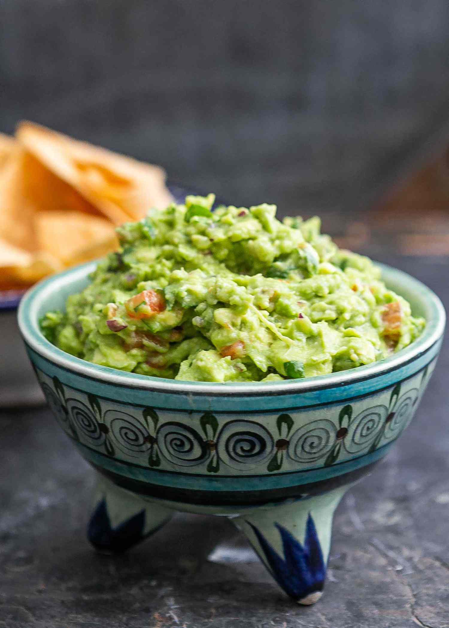 A bowl of homemade guacamole with tortilla chips in the background