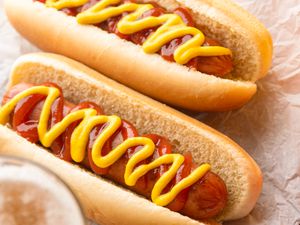 Two hot dogs in buns topped with ketchup and mustard, resting on parchment paper