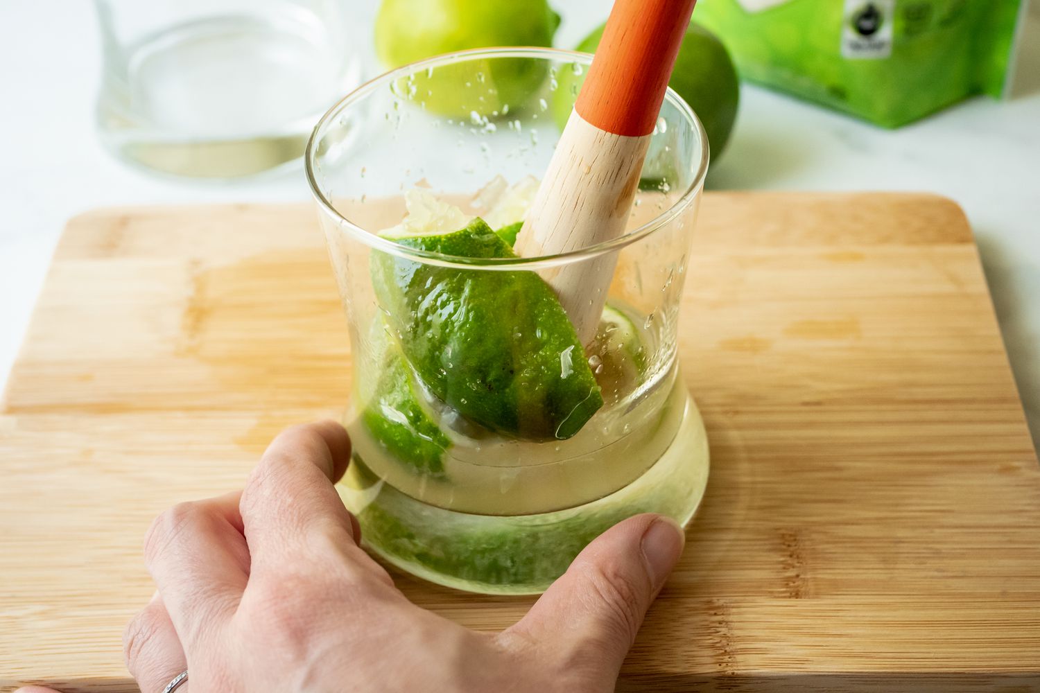Muddling limes and sugar in a rocks glass to make a lime caipirinha cocktail.