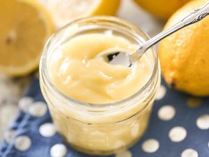 Lemon curd in a jar with a spoon and lemons in the background