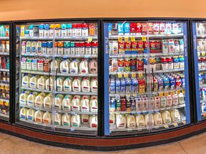 Dairy products displayed in refrigerated sections at a store, including various milk brands in cartons and jugs