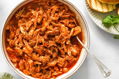 Bowl of Pulled Chicken With a Spoon Next to a Plate With a Toasted Bun and Spinach and a Light Green Table Napkin