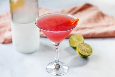 Cosmopolitan ingredients on a counter with a cosmo drink in front.