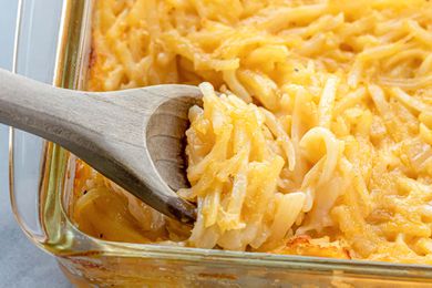 A close up side view of a glass casserole dish with a wooden spoon scooping out the potato casserole.