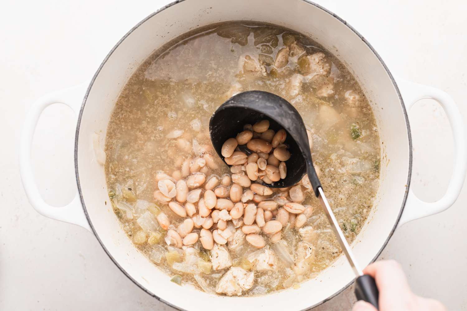 Ladling beans in a pot of chicken chili.
