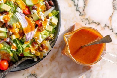 overhead view of a plate of salad with Chipotle Honey Vinaigrette in a small sauce pitcher with a spoon in it