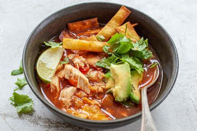 chicken tortilla soup served in a bowl with a spoon, topped with tortilla chips, lime, and cilantro