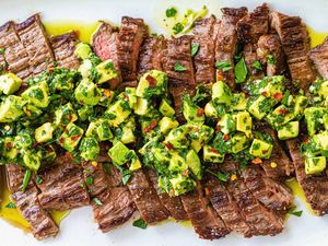 Quick and Easy weeknight skirt steak sliced across the grain and covered with avocado chimichurri on a white plate