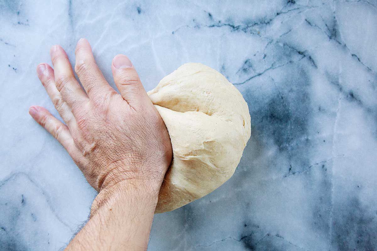 A hand is kneading king cake dough on a marble background.