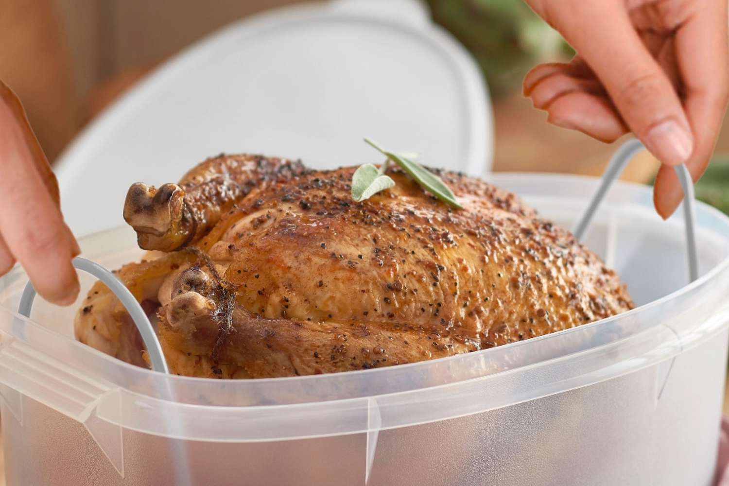 A roasted chicken being placed into a plastic storage container with looped handles