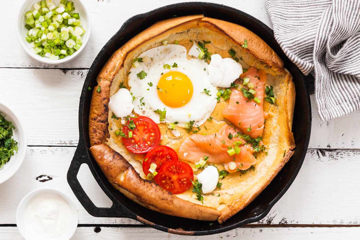 Dutch baby pancake topped with egg, salmon, and tomatoes in a skillet