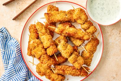 City Chicken, cooked and on skewers on a plate with a creamy sauce on the side in a small bowl