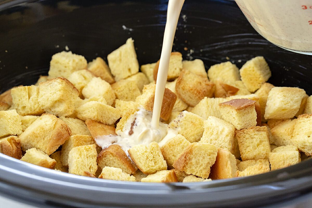 Make Ahead French Toast Casserole - milk being poured over bread cubes in slow cooker