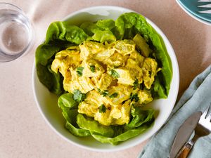 Curry chicken salad served on lettuce leaves in a bowl with forks and a napkin nearby