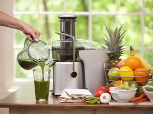 a juicer with fresh fruit and a hand pouring juice into a glass