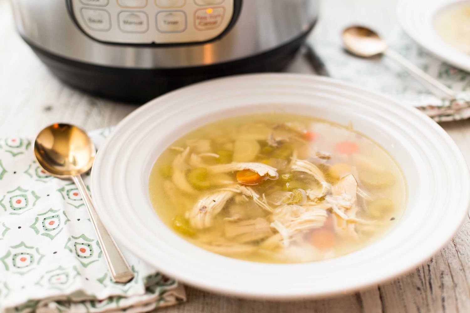 Instant pot chicken noodle soup in a bowl with the instant pot in partial view behind it.