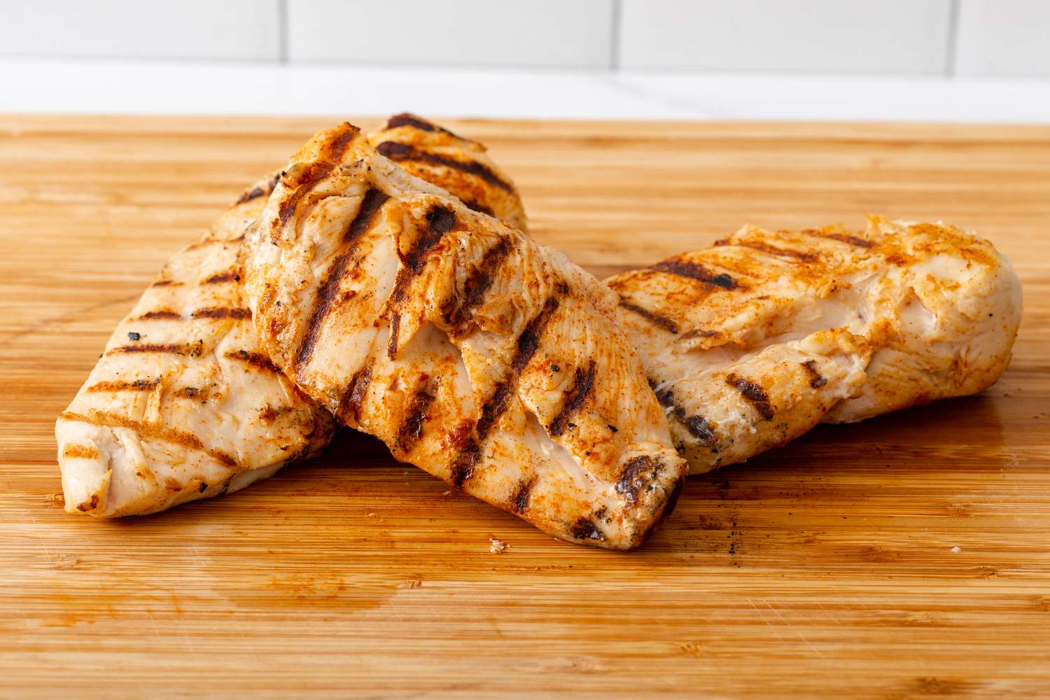 Grilled chicken breast on resting on each other on a cutting board.
