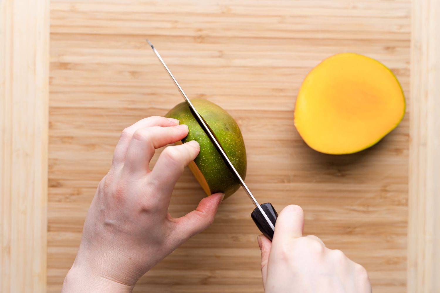 A person cutting a ripe mango.