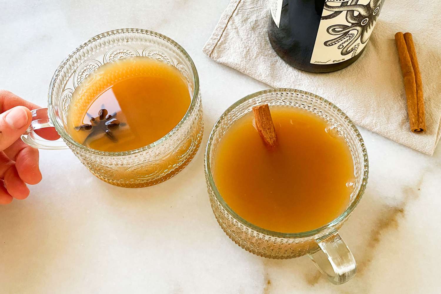 two cups of sider, one garnished with star anise, another garnished with a cinnamon stick