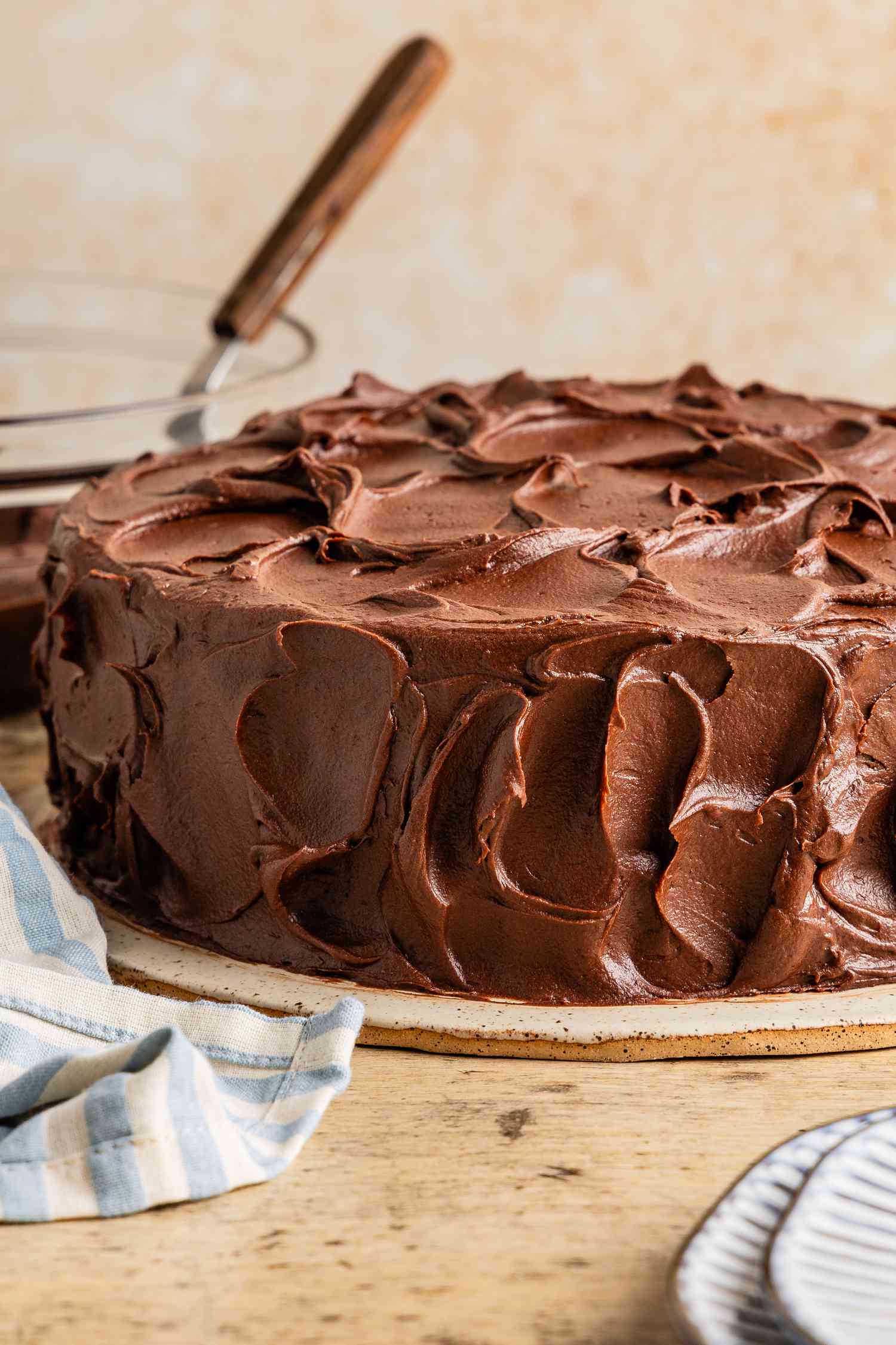 Black magic cake on a plate, and in the background, a bowl of icing