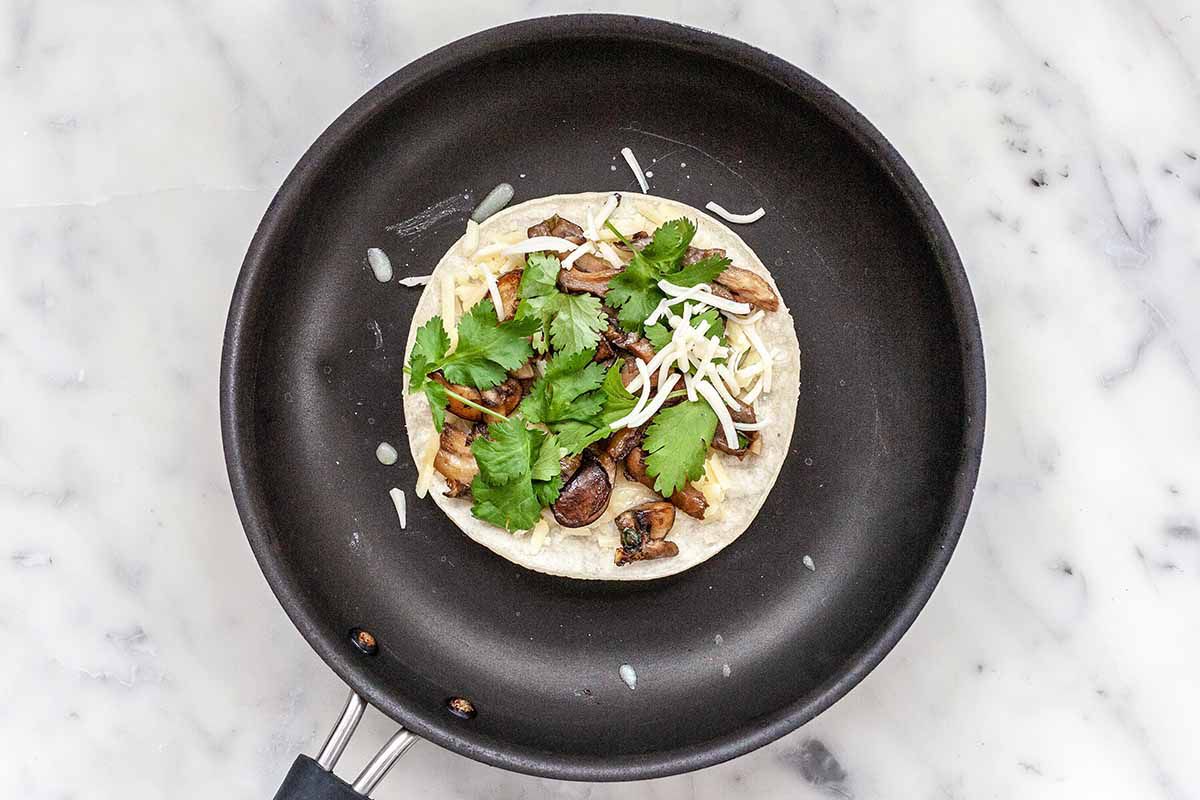 Cheese Quesadilla with Mushrooms - black skillet with quesadilla filled with cilantro, mushrooms and cheese.