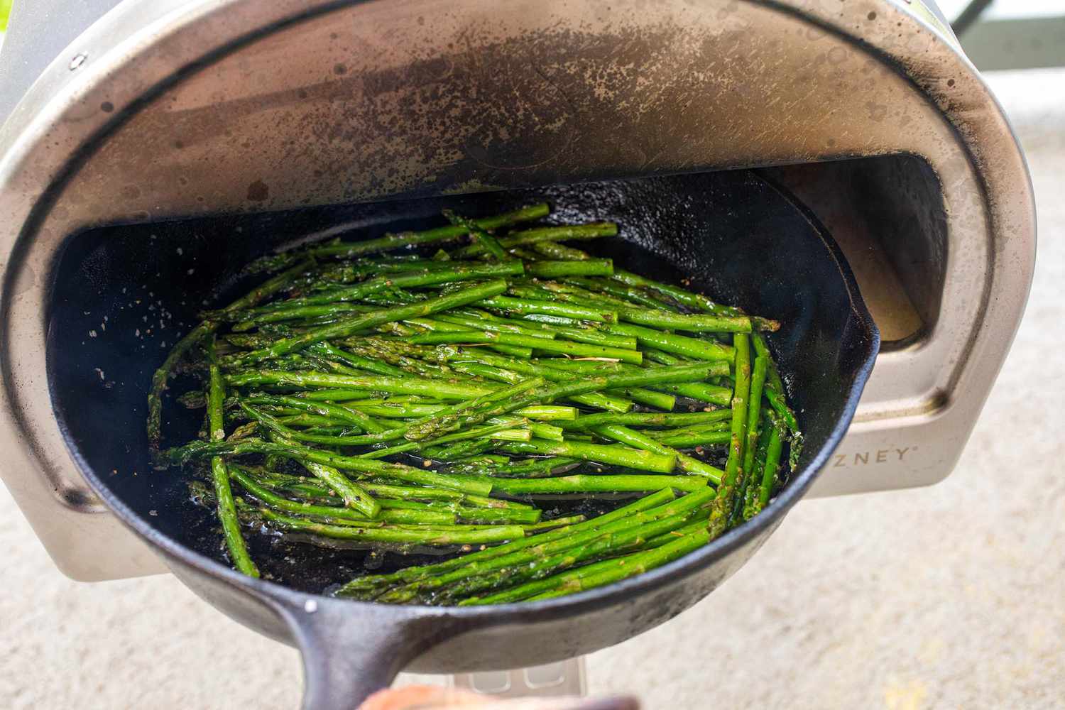 Roccbox pizza oven with a cast iron skillet of asparagus being pulled out of it.