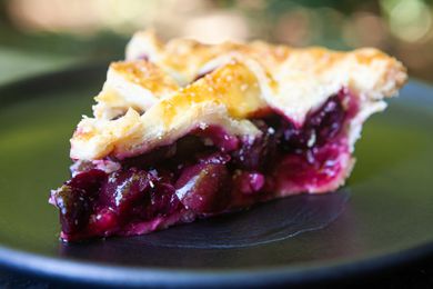 A slice of a cherry pie with a fresh cherry filling visible on the plate.