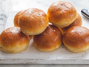 The Fluffiest Brioche Buns stacked on a wood slab.