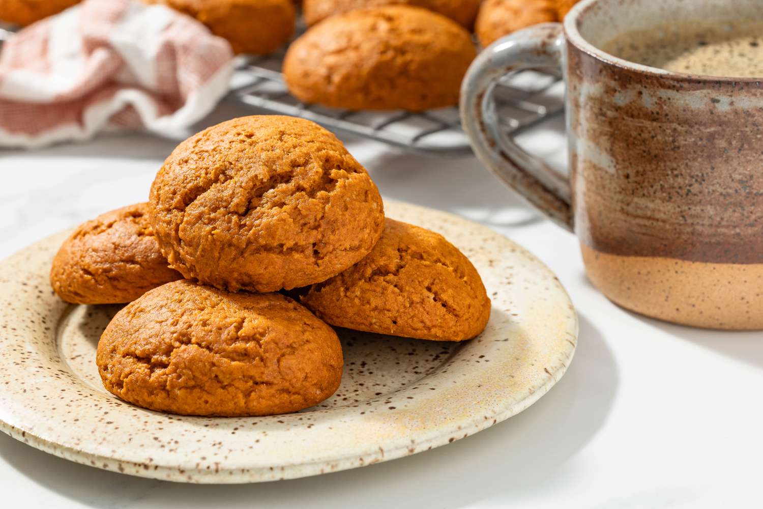 Plate of pumpkin quickies, and in the background, a cup of coffee and more quickies on a cooling rack next to a coral kitchen towel