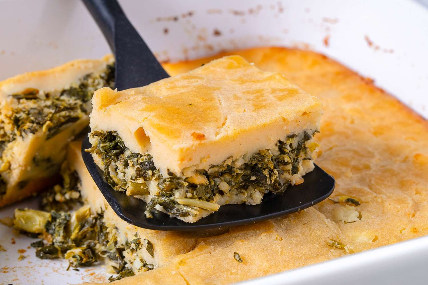 slice of bastaria on a spatula with more in the casserole dish under the spatula